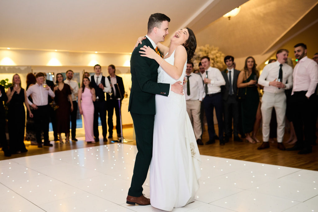 Bride and groom's first dance on a white dance floor, watched by guests