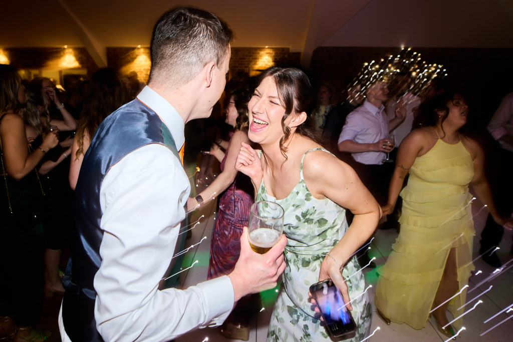 Groom in a waistcoat laughing as he dances with a guest