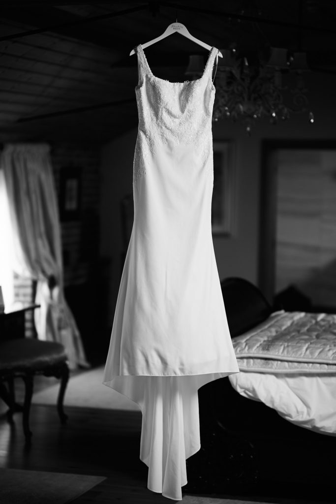 Black and white photo of the wedding dress hanging in a bedroom