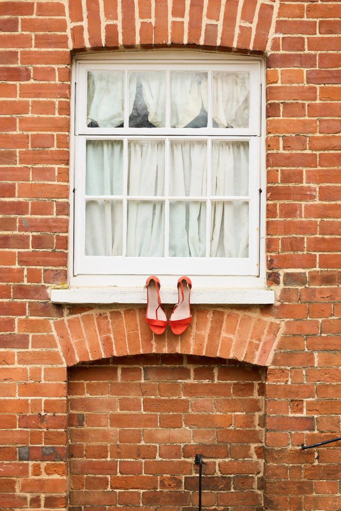Orange bridal shoes on the windowsill of a red-brick building