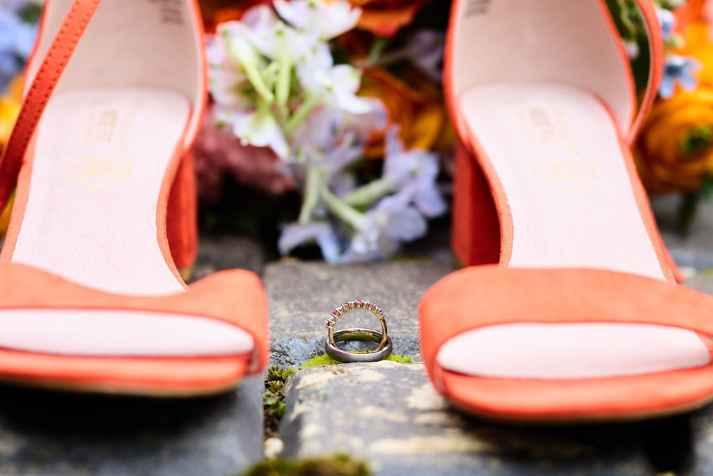 Orange bridal shoes with wedding rings and flowers between them