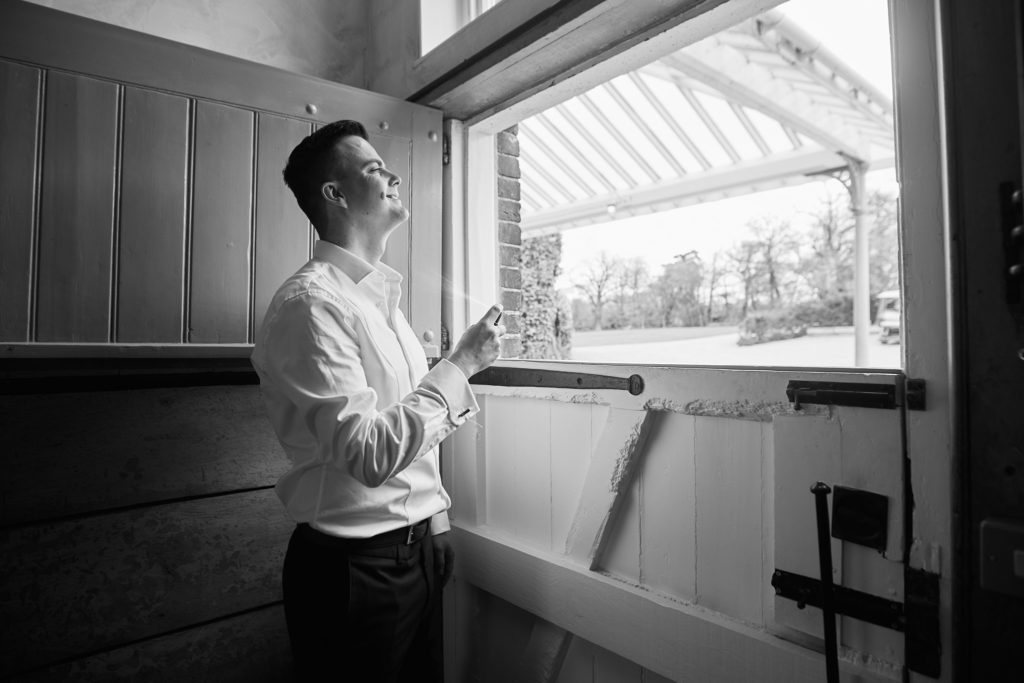 Black and white photo of the groom looking out over a stable door