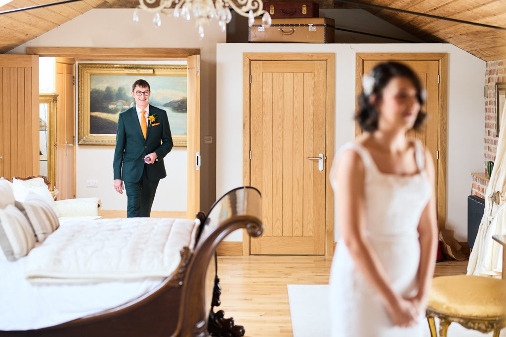 Bride in her wedding dress with a man in a green suit coming through the door behind her