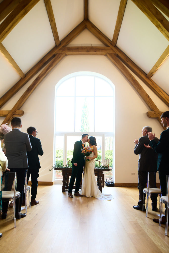 Bride and groom kissing in front of an arched window as guests stand