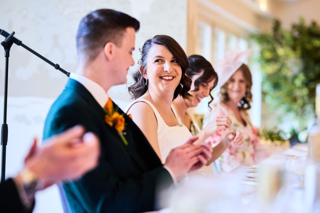 Groom laughing with the bride as he gives his speech