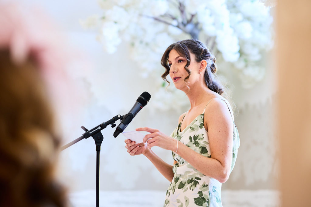 Bridesmaid in a floral dress giving a speech at the microphone
