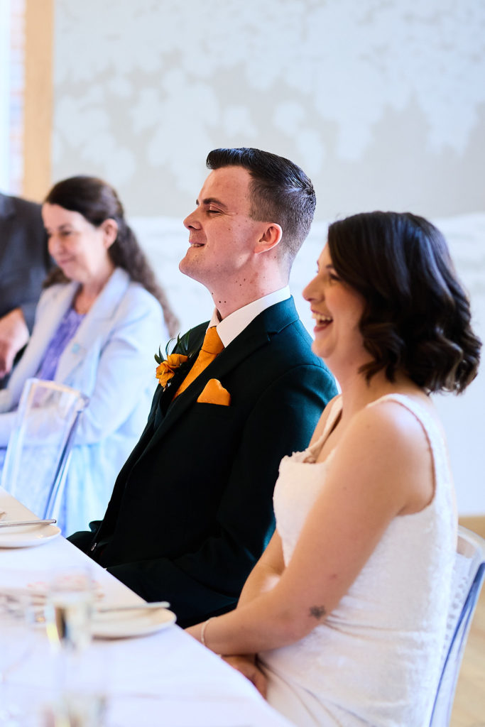 Bride and groom laughing as they listen to the speeches