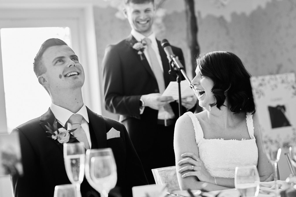 Black and white photo of the groom laughing during the best man's speech