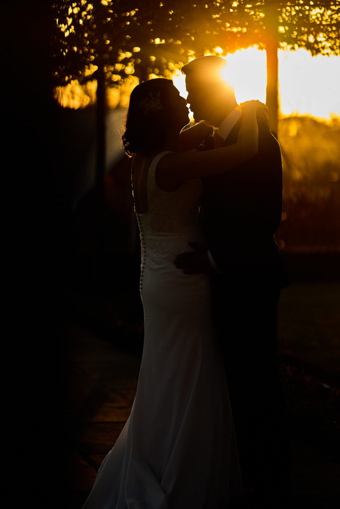 Bride and groom kissing in silhouette against the setting sun at Hatfield Place
