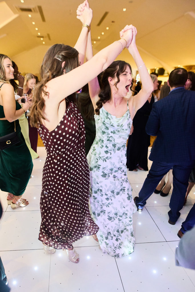Two wedding guests dancing with their hands raised together