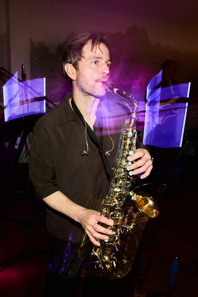 Saxophonist playing among the guests under purple lights
