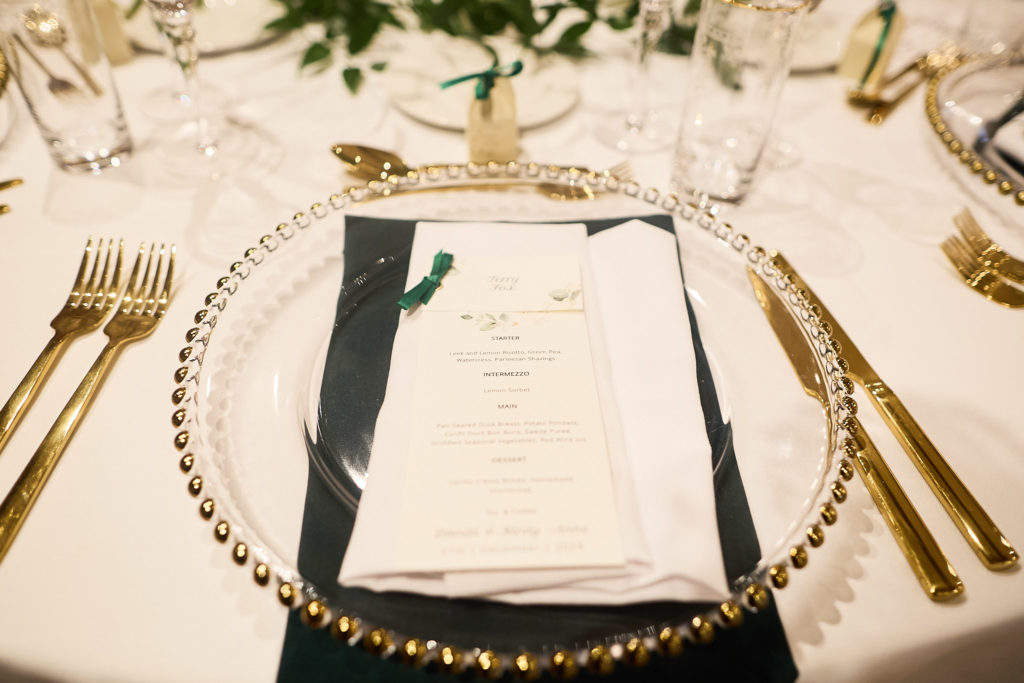 Place setting with a gold-rimmed glass charger, gold cutlery and a dark green napkin
