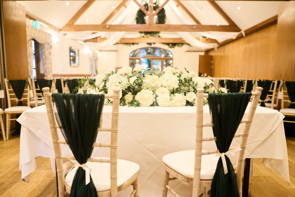 Top table with white flowers and chairs tied with dark green sashes at Mulberry House