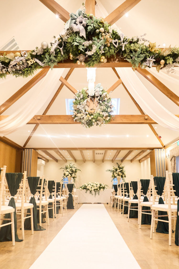 Ceremony room with oak beams, a white aisle and hanging flower wreaths at Mulberry House