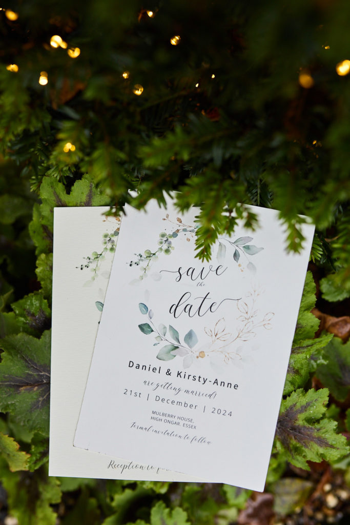 Save the date cards hanging among green leaves and fairy lights