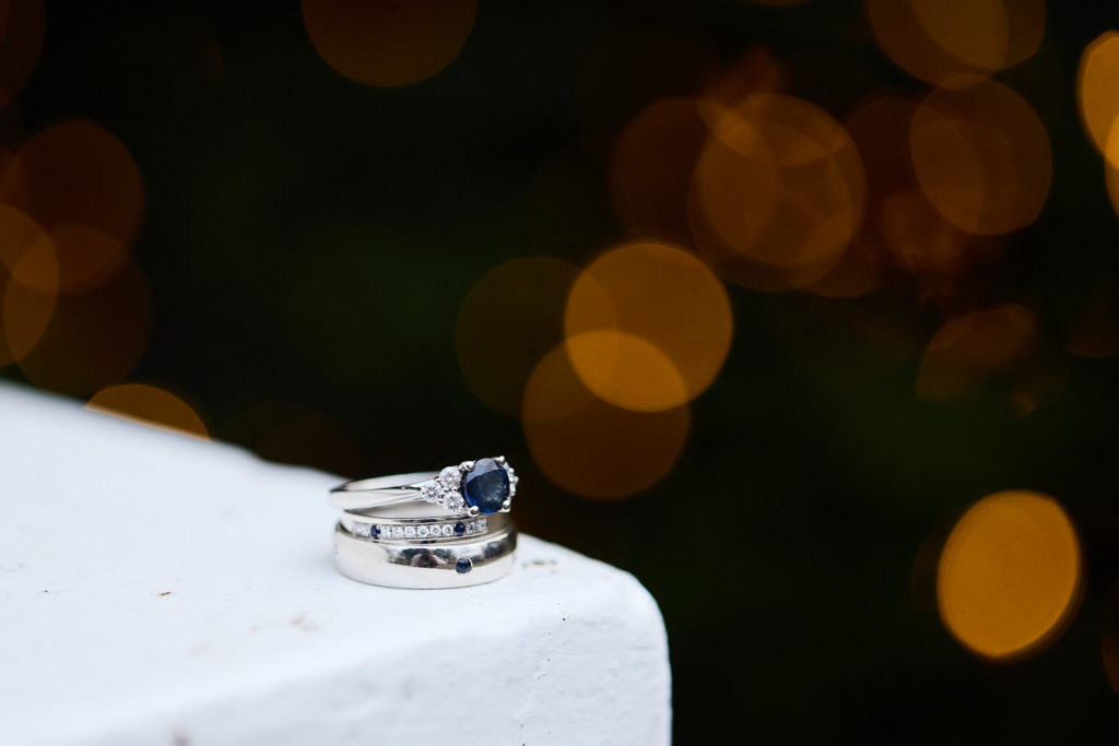 Wedding rings on a white surface with fairy lights glowing behind