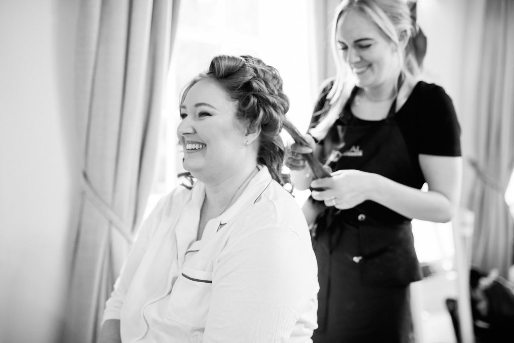 Bride laughing as her hair is styled on the wedding morning