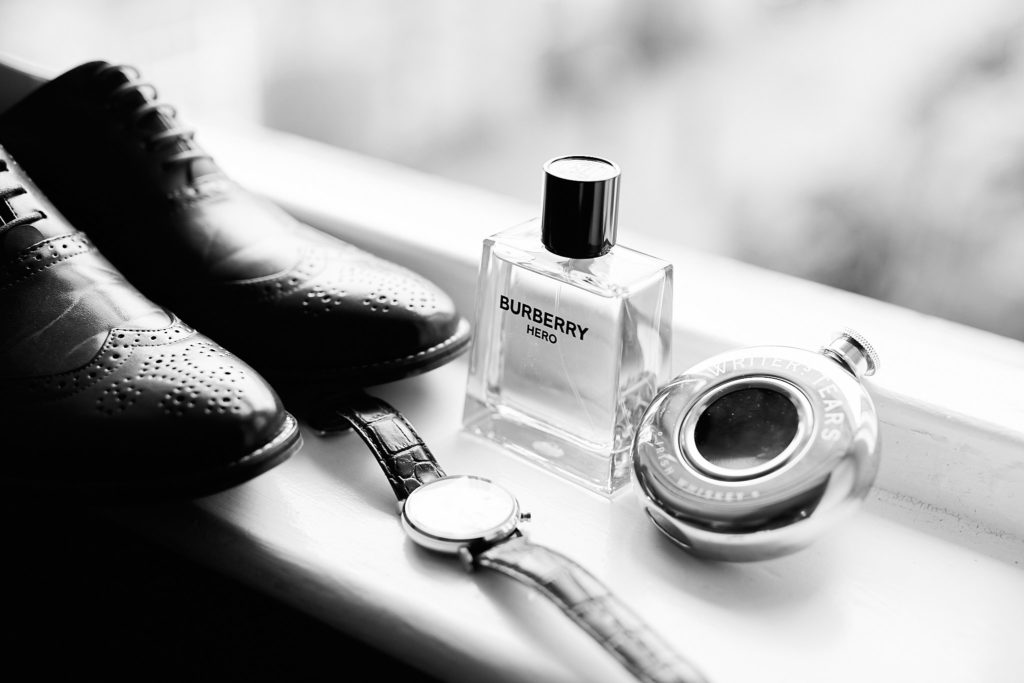 Black and white photo of the groom's shoes, watch and aftershave on a windowsill