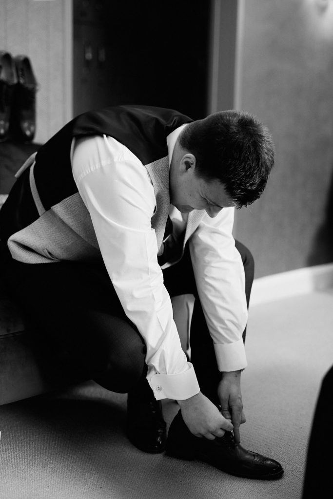 Black and white photo of the groom tying his shoelaces
