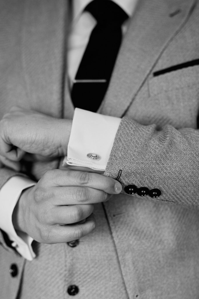Black and white close-up of the groom fastening his cufflink