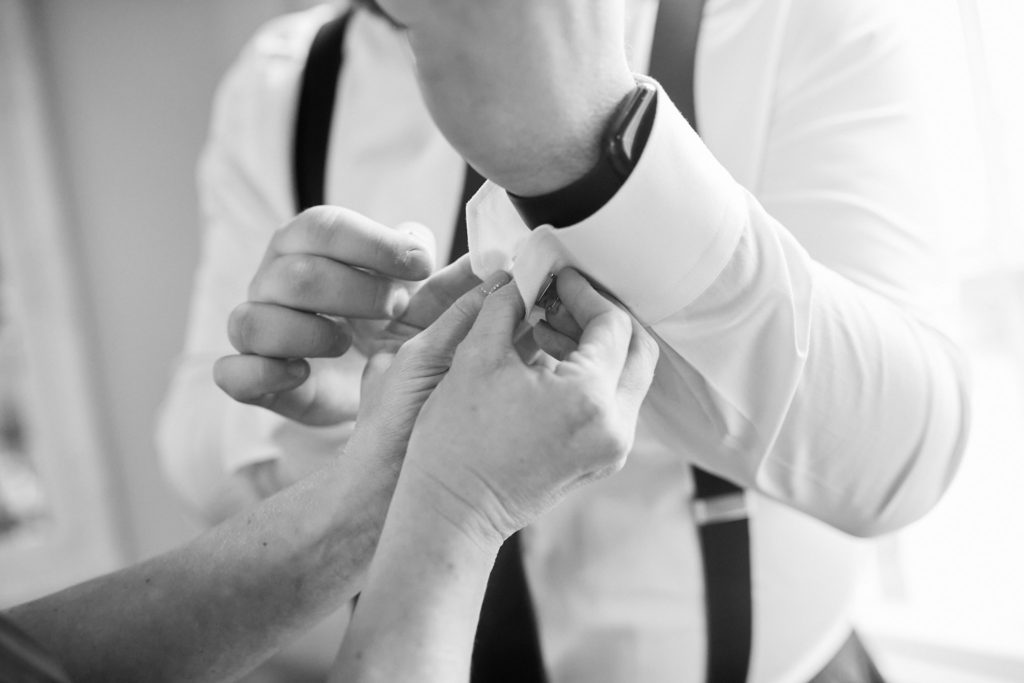 Black and white close-up of the groom fastening his shirt cuff