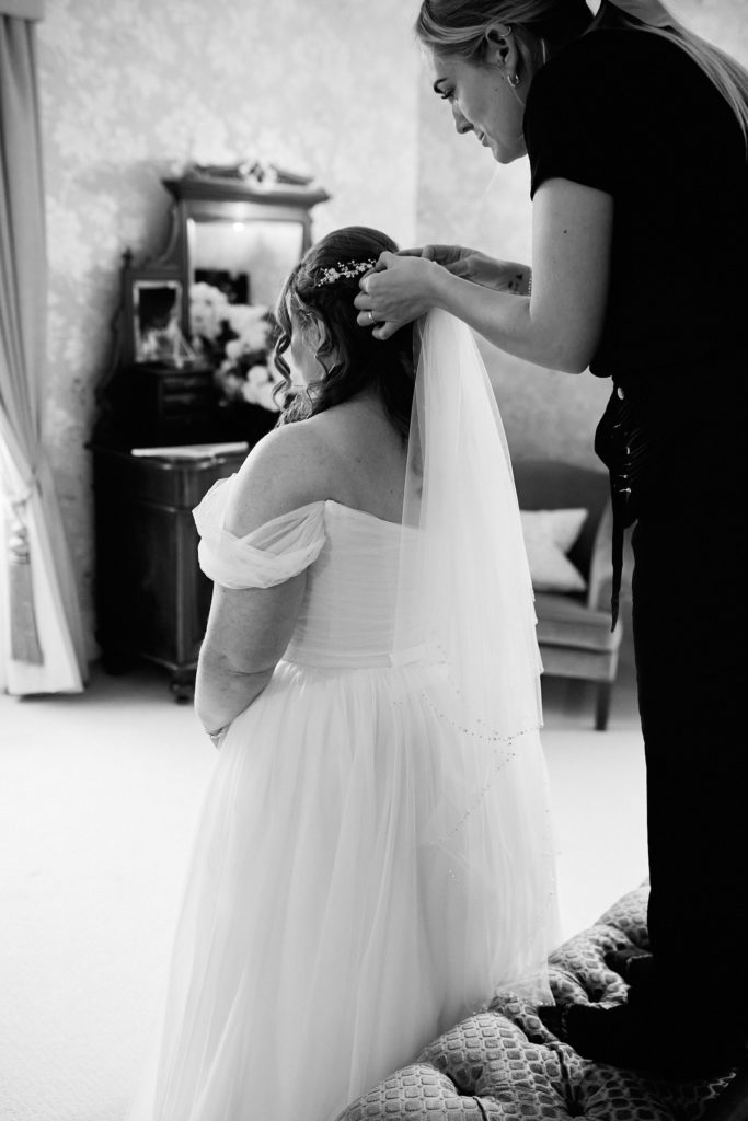 Black and white photo of the bride having her veil pinned in place