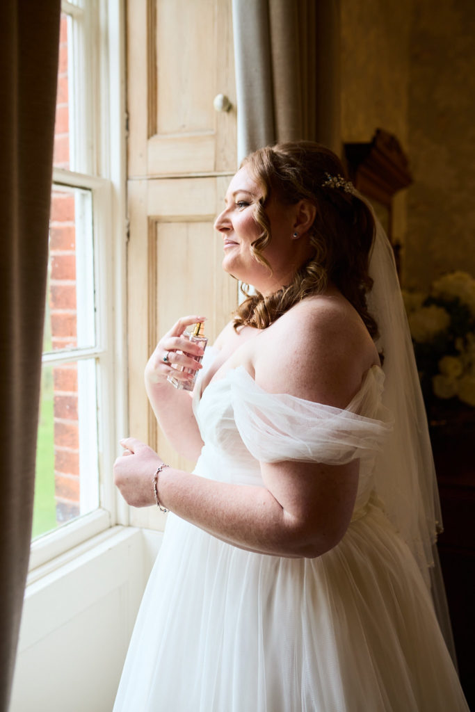 Bride laughing beside a window in her off-the-shoulder wedding dress