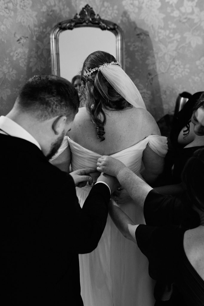 Black and white photo of the back of the bride's dress being fastened