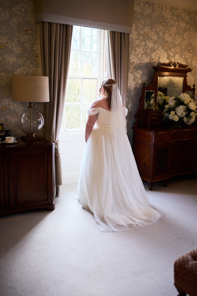 Bride from behind looking out of a window in her wedding dress at Mulberry House