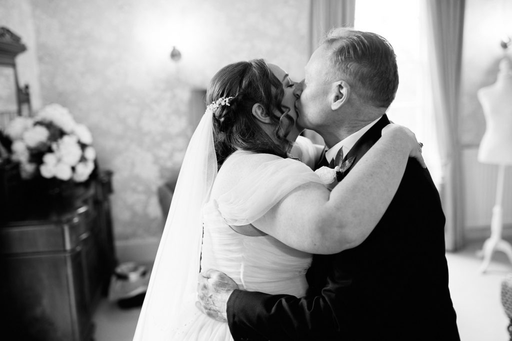 Black and white photo of a man kissing the bride on the cheek before the ceremony
