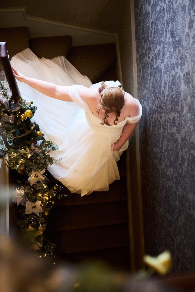 Bride seen from above coming down a staircase trimmed with Christmas garlands