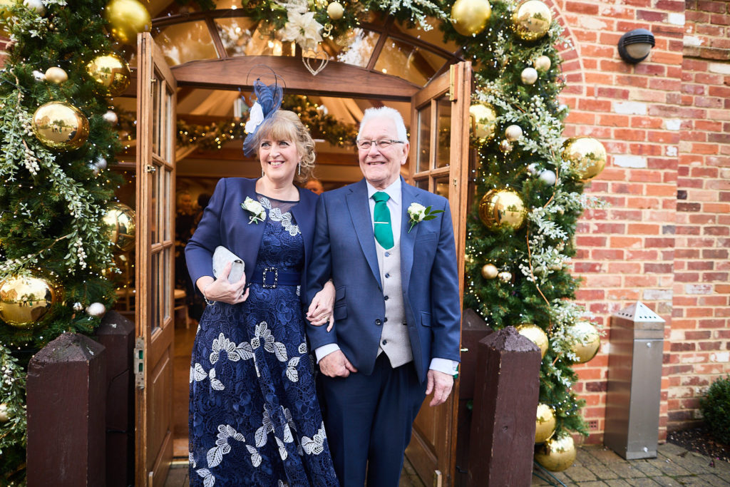 Older couple arriving through a doorway decorated with Christmas garlands and gold baubles