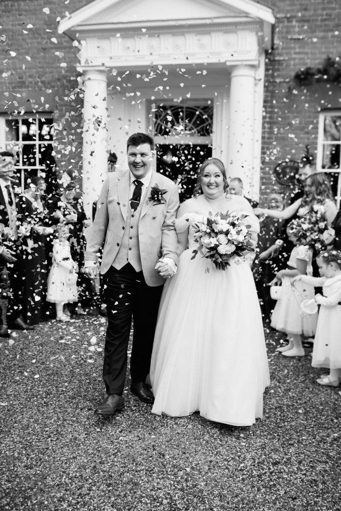 Black and white photo of the bride and groom walking through confetti outside Mulberry House