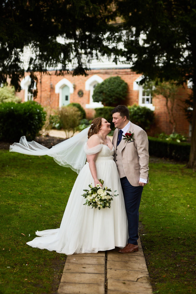 Bride and groom laughing as her veil blows in the wind in front of Mulberry House