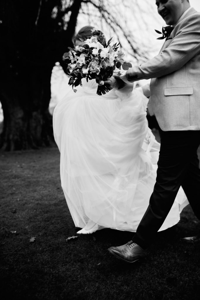 Black and white photo of the groom carrying the bride's dress train