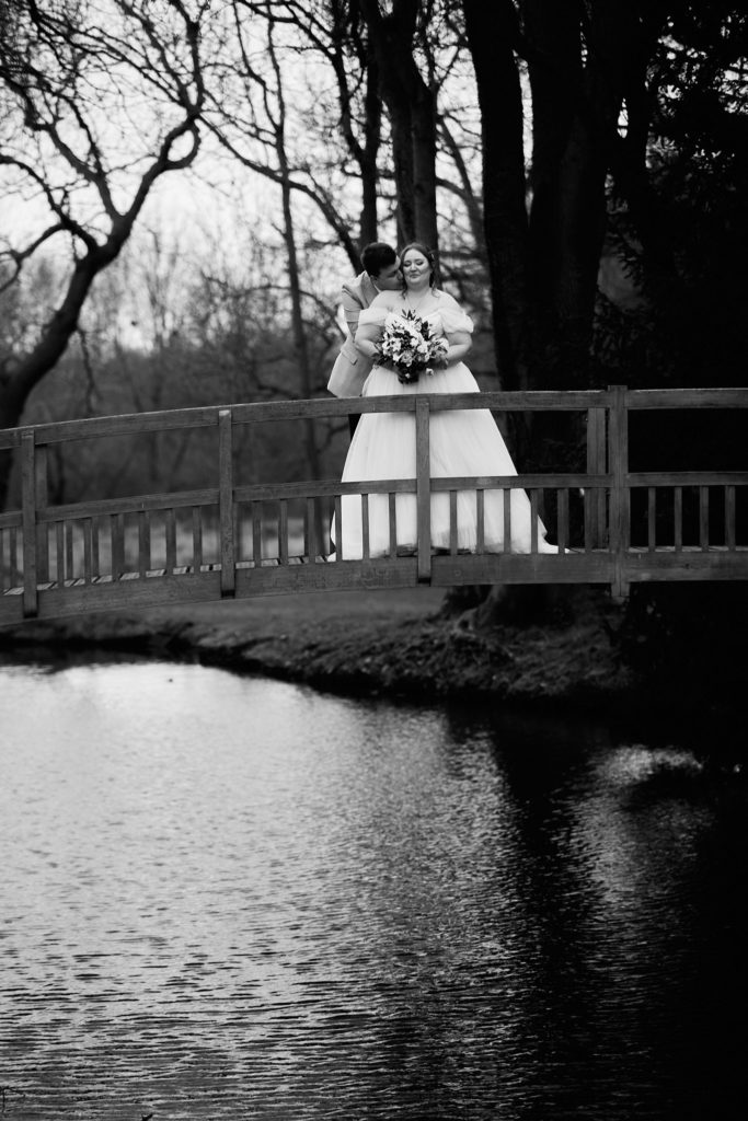 Black and white photo of the bride on the wooden bridge at Mulberry House, reflected in the water