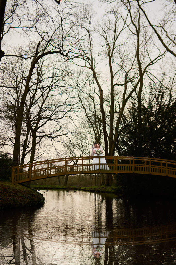 Bride and groom on the bridge beneath bare winter trees at Mulberry House