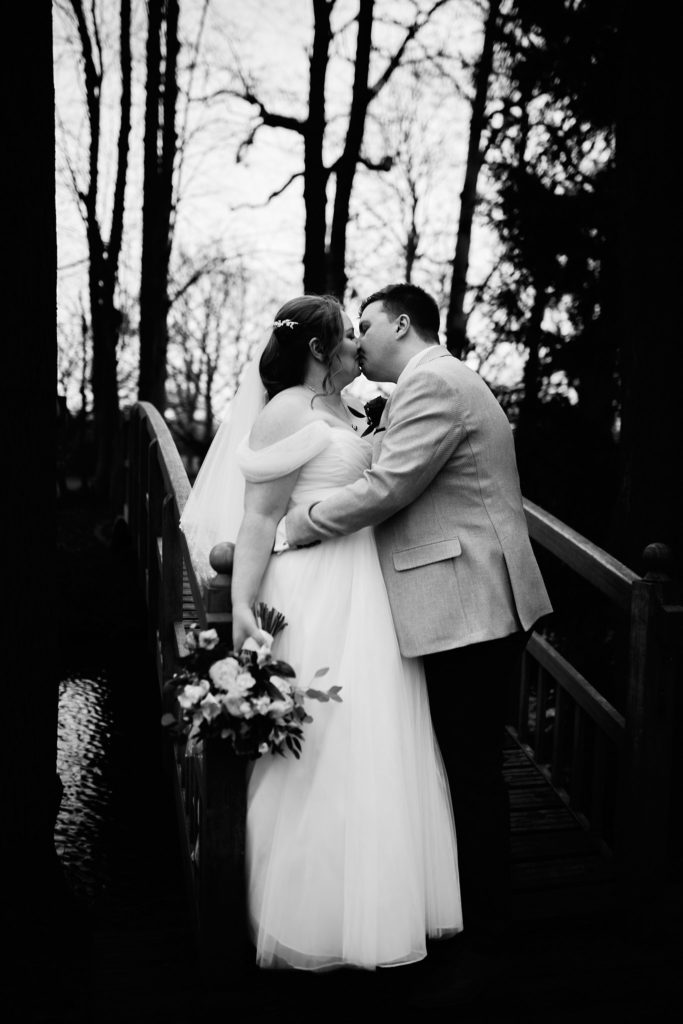 Black and white photo of the bride and groom kissing on the bridge at Mulberry House