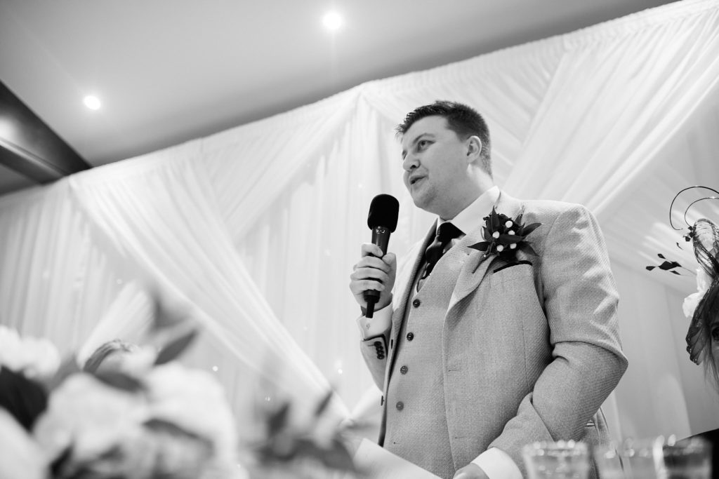 Black and white photo of the groom giving his speech with a microphone