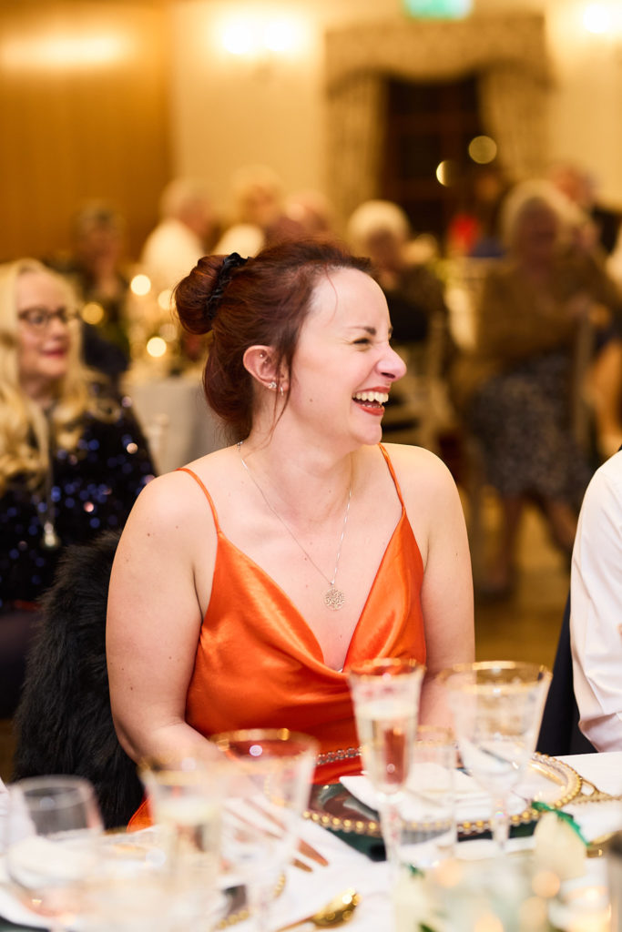 Wedding guest in an orange dress laughing during the speeches
