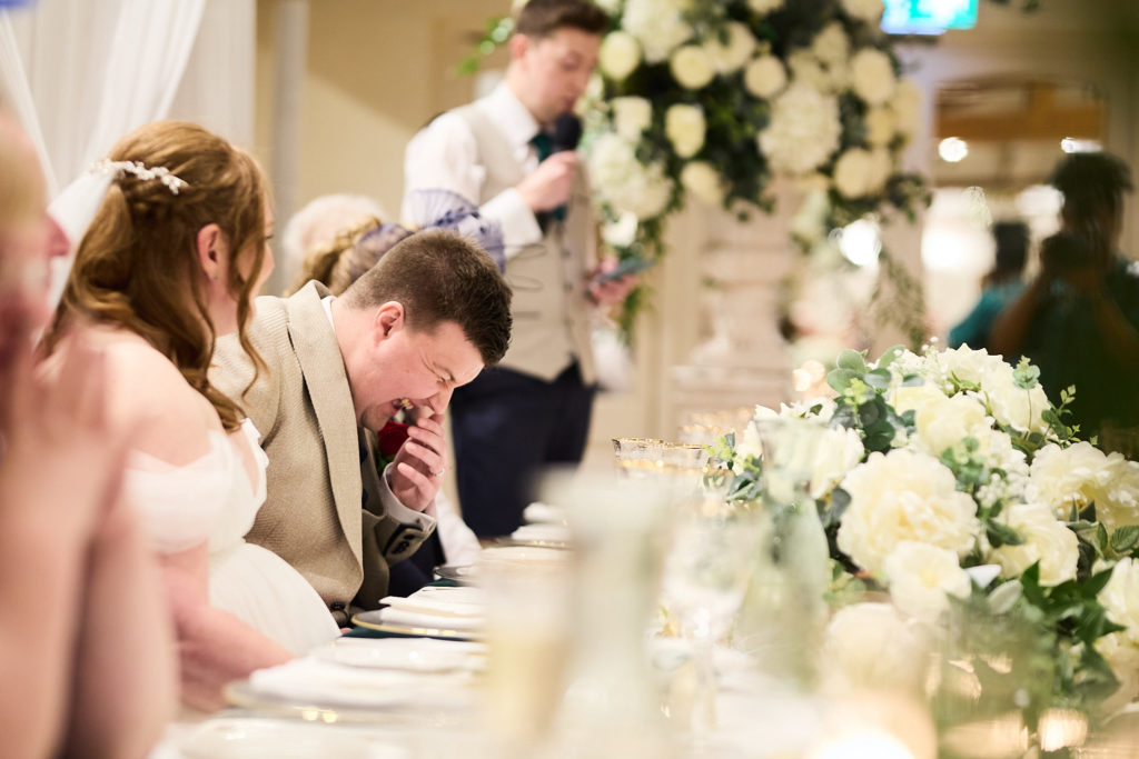 Bride and groom hiding their faces as they laugh during a speech