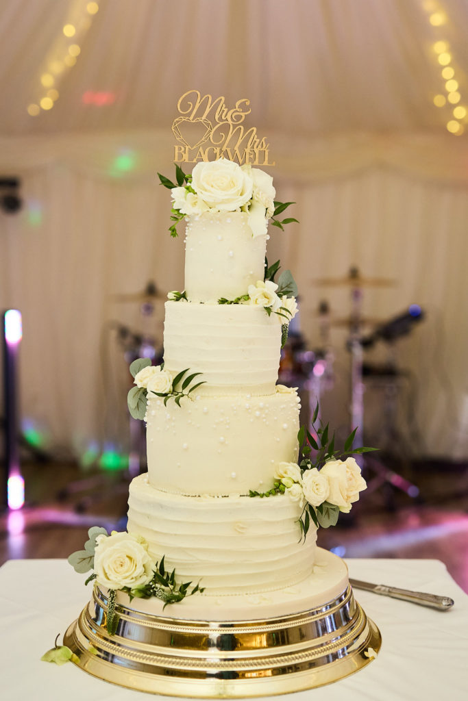 Four-tier white wedding cake decorated with white roses