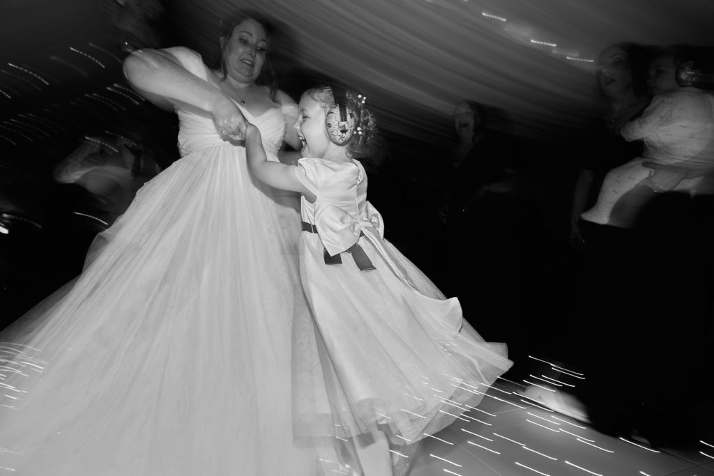 Black and white photo of the bride spinning a child round on the dance floor