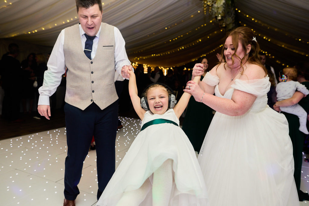 Bride and groom swinging a young bridesmaid between them on the dance floor