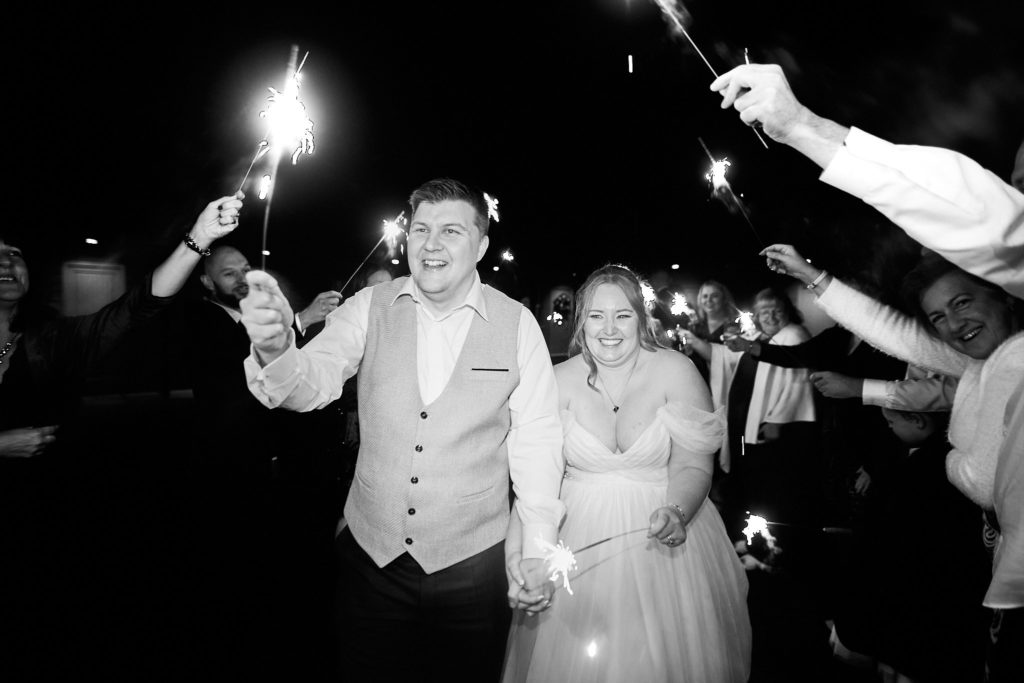 Black and white photo of the bride and groom walking through a tunnel of sparklers