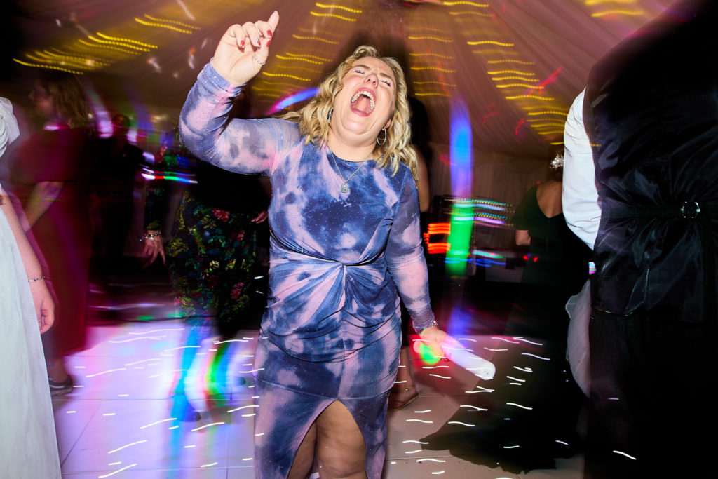 Wedding guest in a blue dress dancing with her arm raised
