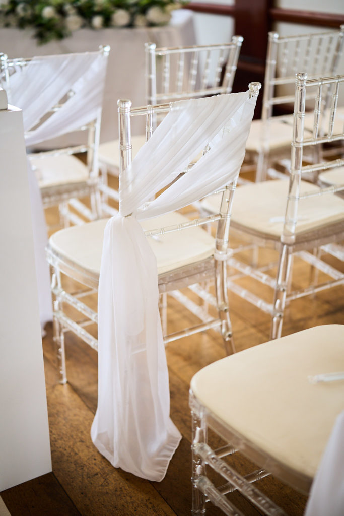 Clear ceremony chairs tied with white fabric sashes