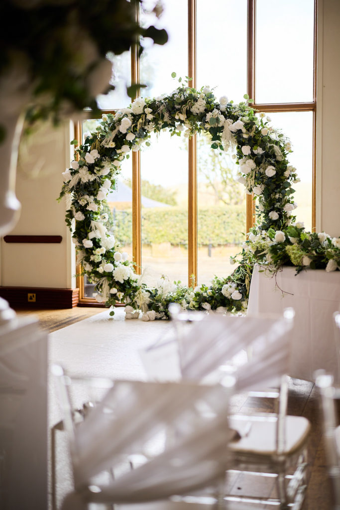 Circular arch of white flowers and greenery beside a window at Stock Brook Manor