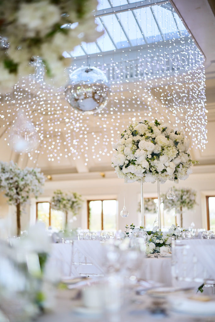 Reception room with a fairy-light ceiling, mirror ball and tall white floral centrepieces