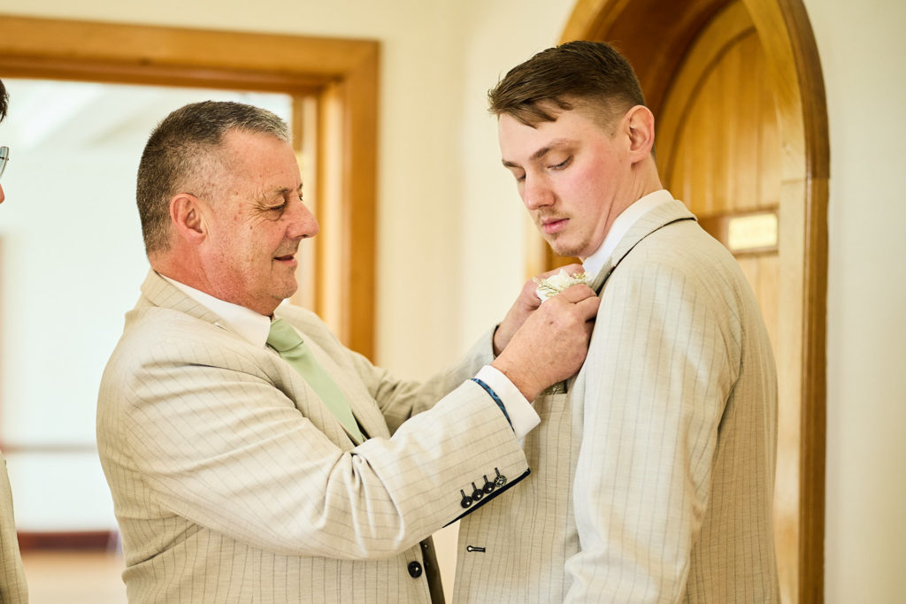 Man in a cream suit pinning on the groom's buttonhole